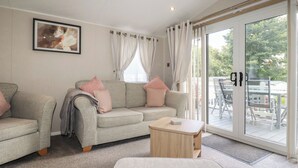 Ein gemütliches Wohnzimmer mit einem grauen Sofa, einem kleinen Holztisch und einer großen Schiebeglastür, die zu einem Außenbereich führt.