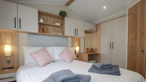 Ein ordentlich eingerichtetes Schlafzimmer mit Bett, zwei Kissen, einem Nachttisch, einem Kleiderschrank und einem Regal mit Dekoration.