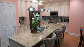 Una cocina con encimera de granito, un fregadero, microondas y estufa. Hay luces colgantes sobre la encimera y una planta en maceta en la isla.