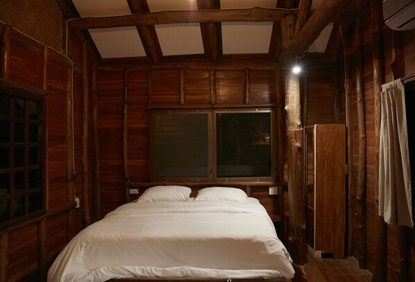 A wooden cabin-style room with a large bed, a window, and a ceiling with exposed beams.