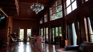 A spacious room with a wooden floor, large windows, a chandelier, and a dining area. - NUYU Khaoyai (Pak Chong)