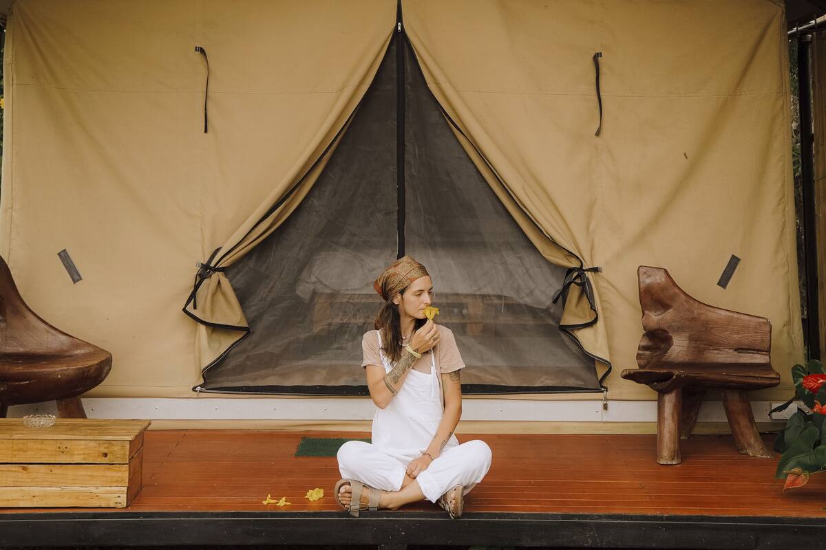 A person sitting on a wooden bench in front of a tent-like structure with a wooden bench to the right.