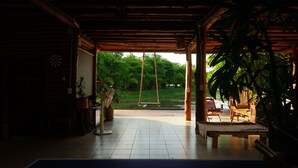 A covered outdoor area with a swing, a bench, and a view of greenery. - NUYU Khaoyai (Pak Chong)