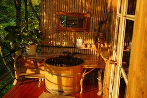 Uma cabana rústica de madeira com um deck de madeira, um barril grande de madeira e plantas em vasos.