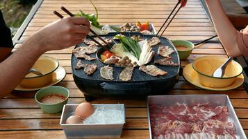 A wooden table with a black grill, various meats, vegetables, and condiments.