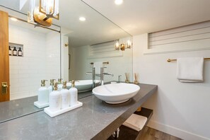 A modern bathroom with a large mirror, a round sink, and a vanity with toiletries. - Aspen Valley Sky Ranch (Carbondale)