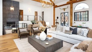A spacious living room with a fireplace, a staircase, and a large window. - Aspen Valley Sky Ranch (Carbondale)