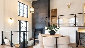 A spacious living area with a round table and ottomans, a fireplace, and a view of the outdoors through large windows. - Aspen Valley Sky Ranch (Carbondale)