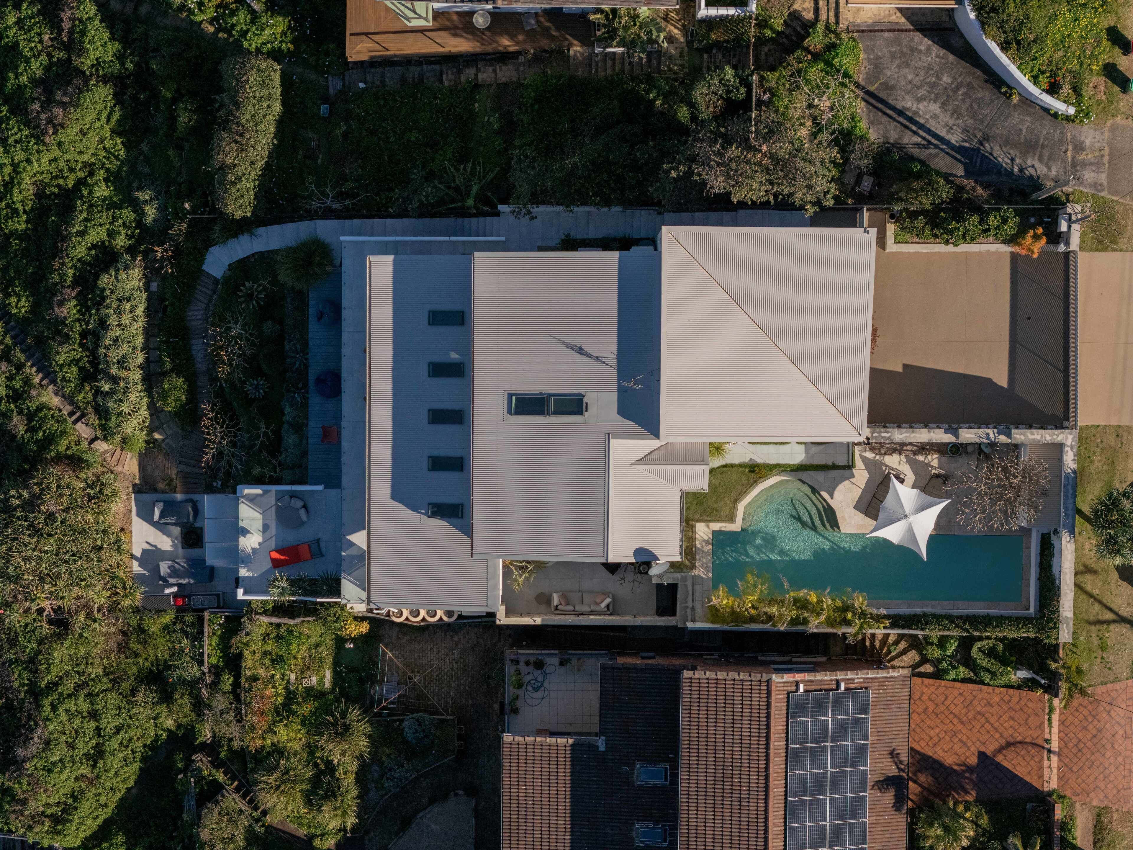 An aerial view of a modern house with a swimming pool, a covered patio, and a solar panel.