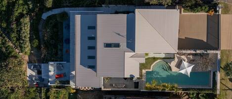 An aerial view of a modern house with a swimming pool, a covered patio, and a solar panel.
