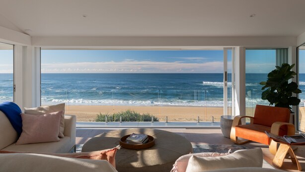 Un saló modern amb una finestra gran que dona a una platja, una zona de seients còmoda i vista a l'oceà.