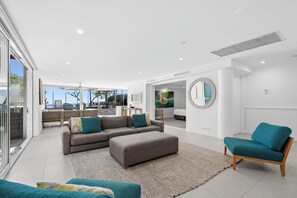 Ampla sala de estar com sofá modular, um espelho redondo e vista para o exterior.