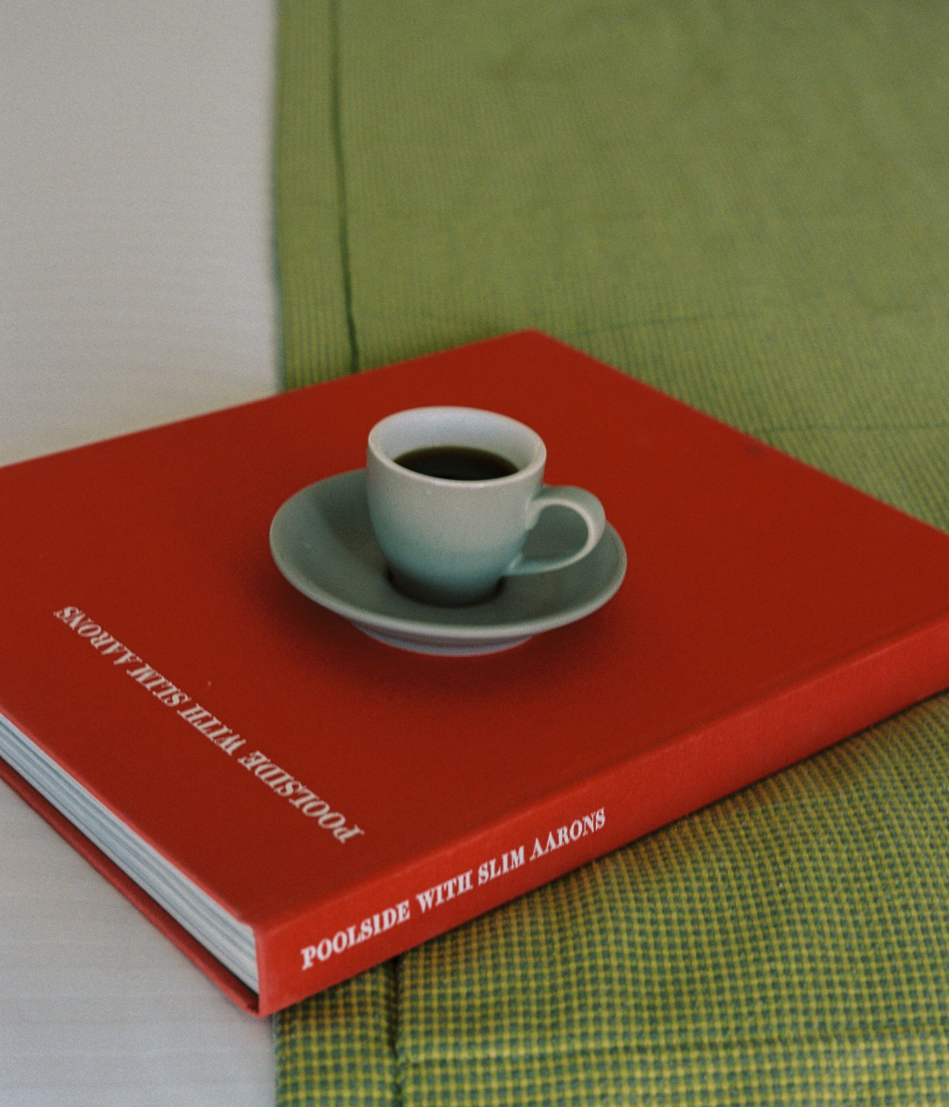 Un libro titulado "POOLSIDE WITH SLIM AARONS" con una taza de café encima.