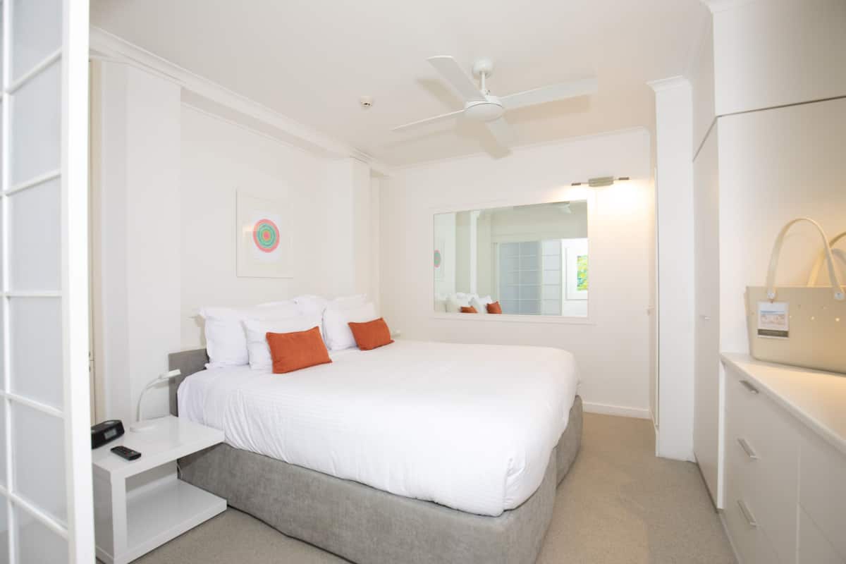 A bedroom with a bed, a nightstand, a mirror, a ceiling fan, and a dresser.