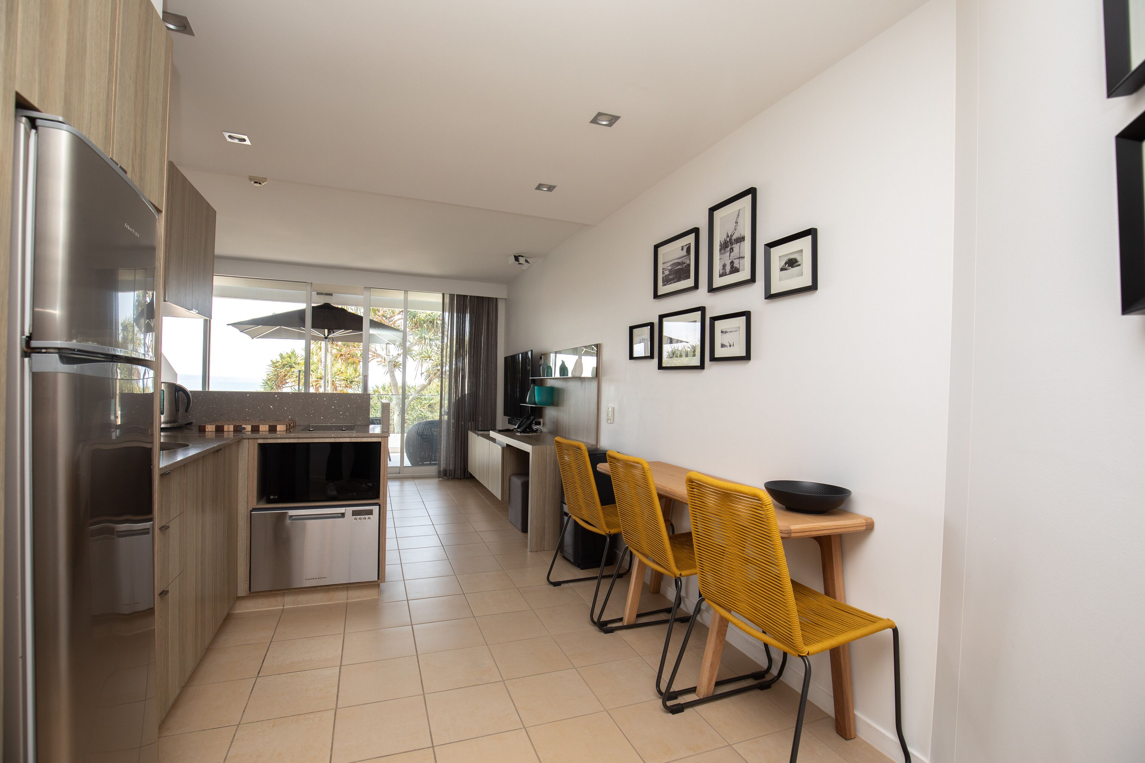 Une cuisine moderne dotée d’appareils électroménagers en acier inoxydable, un coin repas avec des chaises jaunes et une vue à travers la porte vitrée.