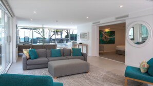 A modern living room with a grey sectional sofa, teal armchairs, and a large window overlooking a dining area. - 71 Hastings Street - Beachfront (Noosa Heads)
