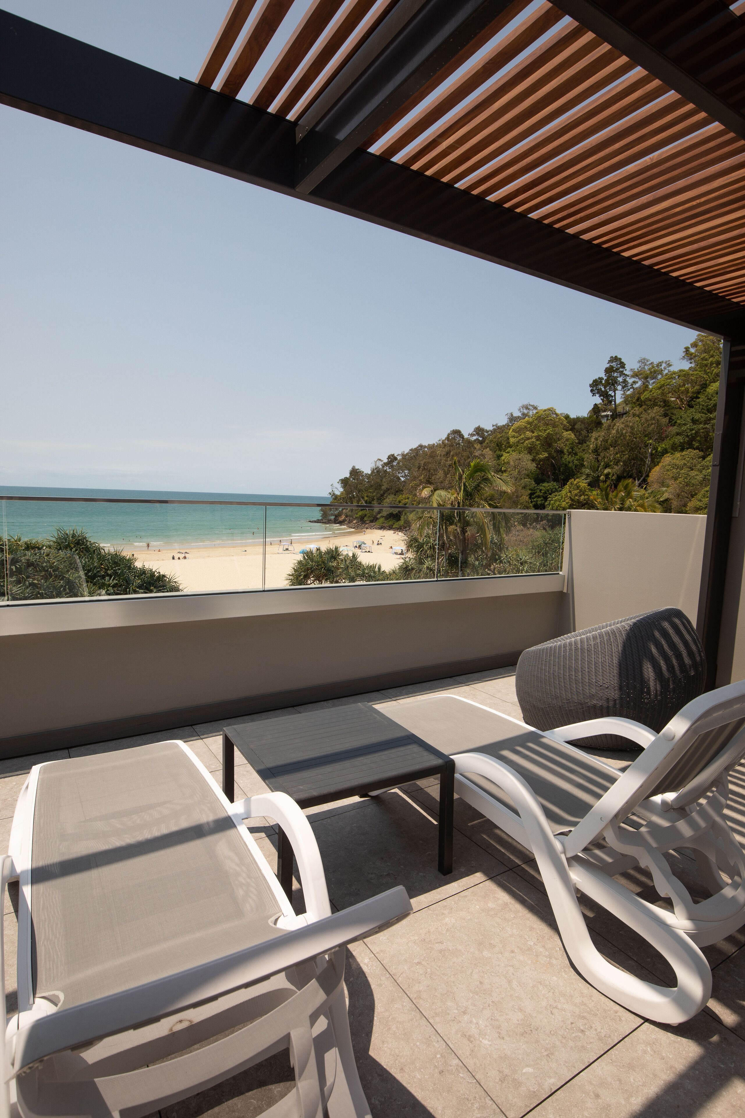 A balcony with two white lounge chairs, a small table, and a view of the beach and ocean.