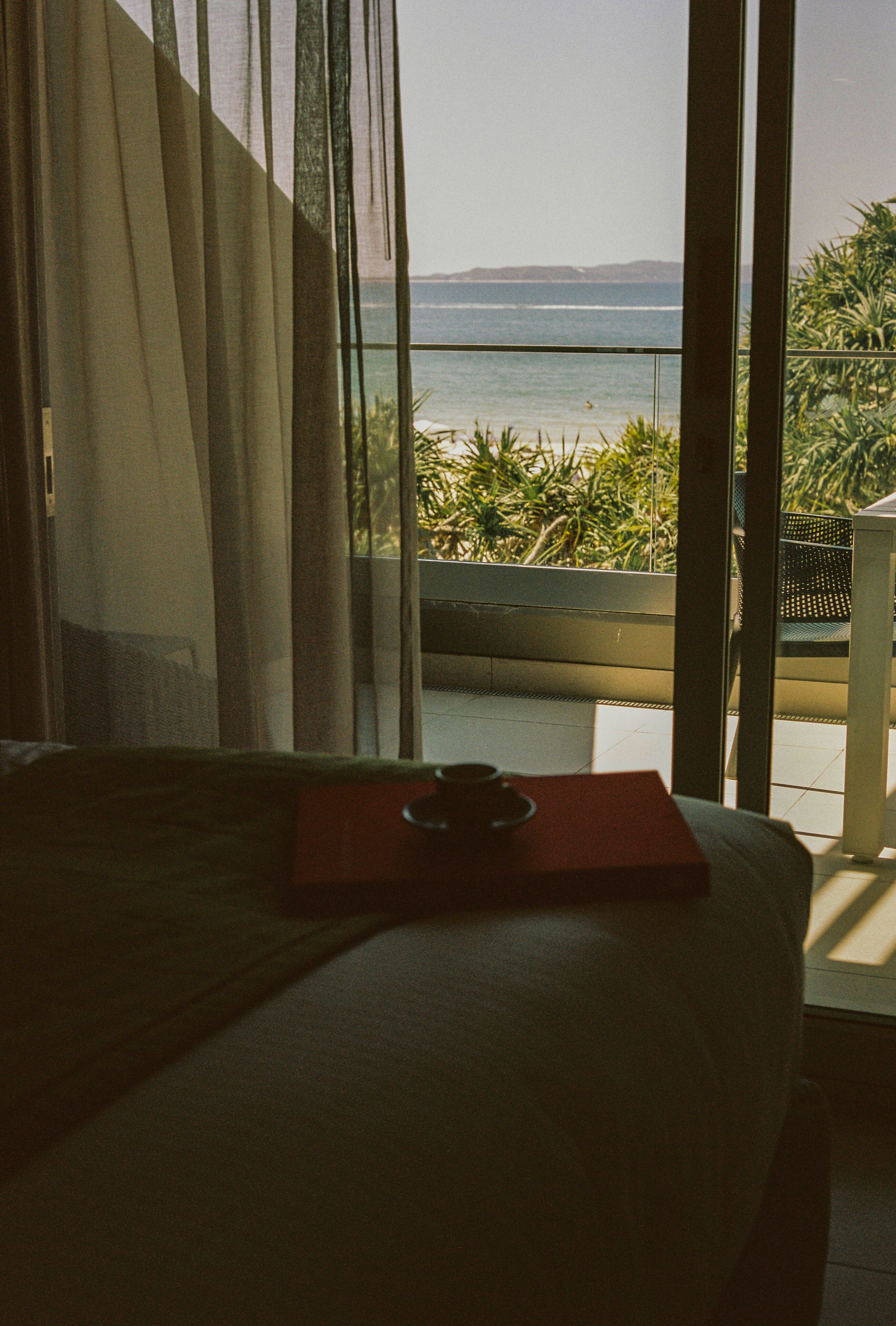Ein Zimmer mit einem Bett, einem Vorhangfenster und Blick aufs Meer.