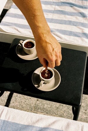 A hand stirring two cups of coffee on a small table. - 71 Hastings Street - Beachfront (Noosa Heads)