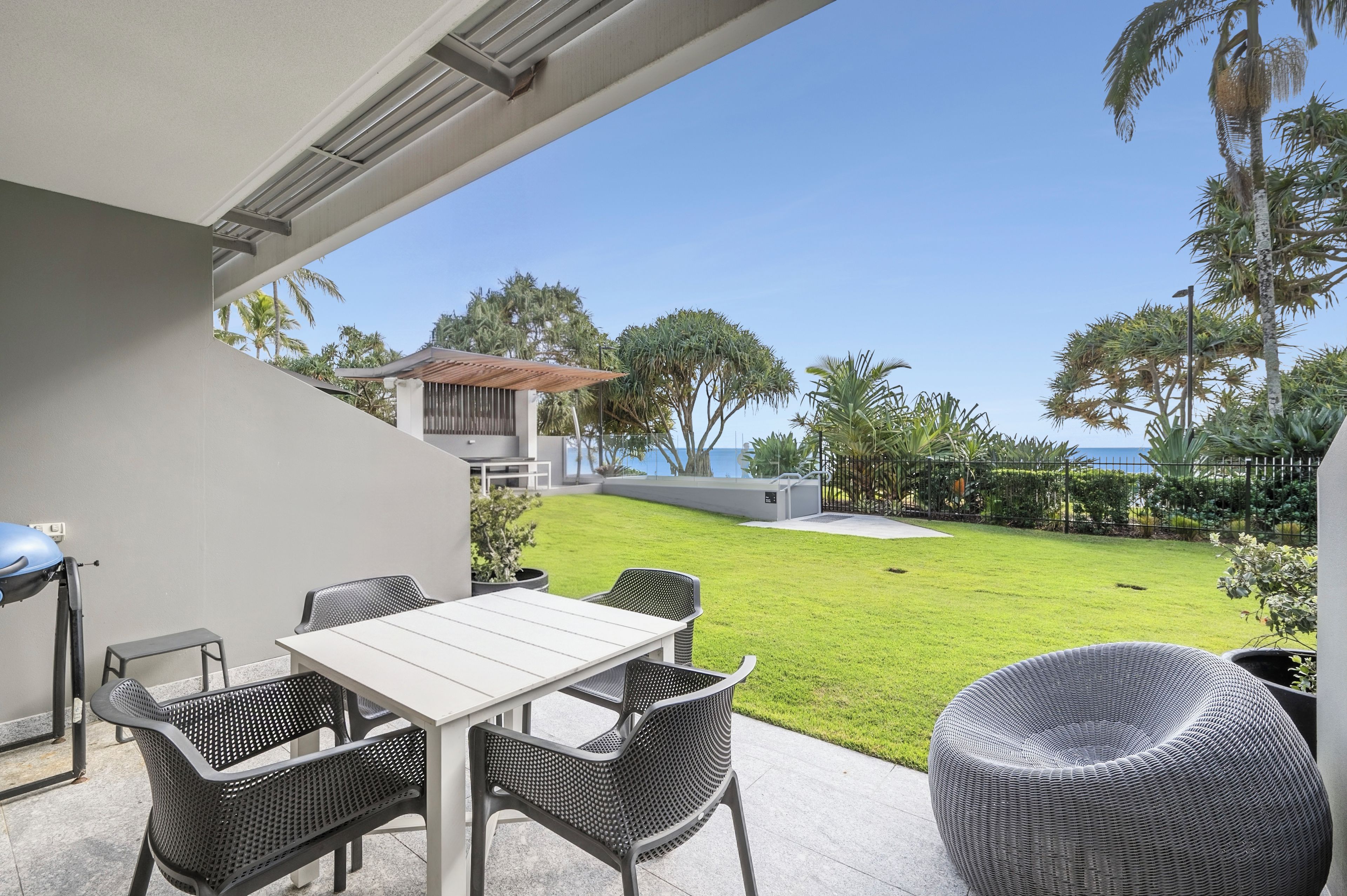 An outdoor patio with a table and chairs, a view of a well-maintained lawn, and a distant building.