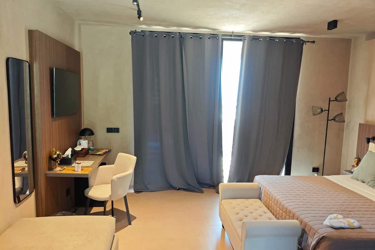 Ein Hotelzimmer mit Bett, Schreibtisch mit Stuhl, Fernseher und einem großen Fenster mit Vorhängen.