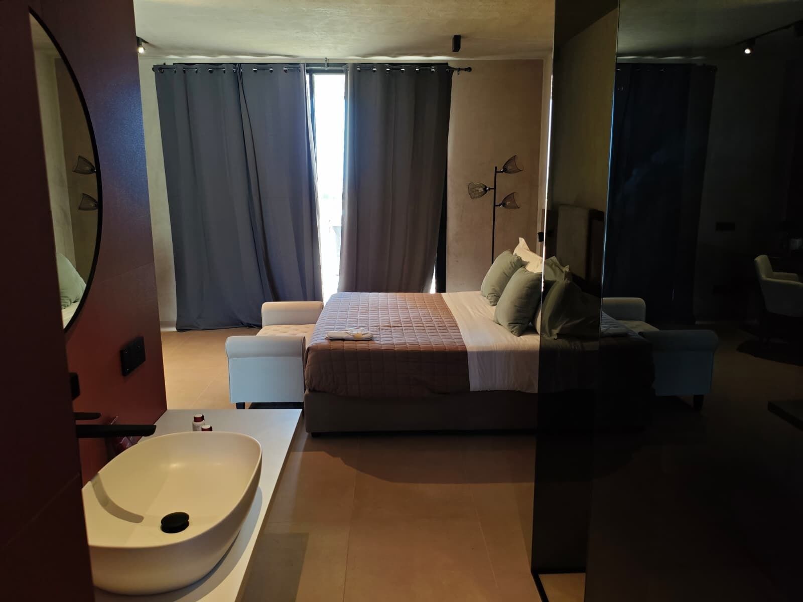 Een moderne slaapkamer met een groot bed, een nachtkastje, een witte wastafel en een spiegel.