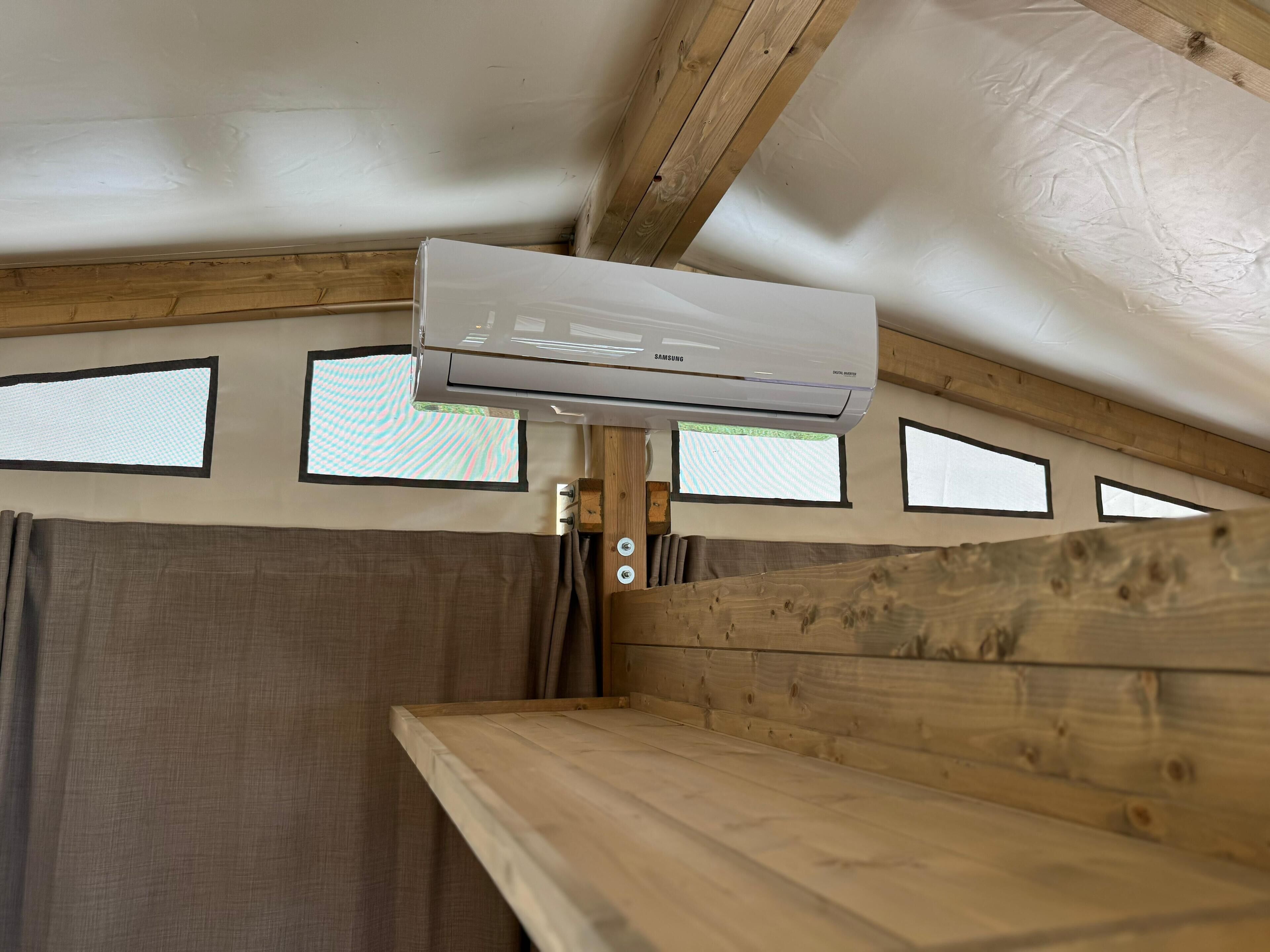 Una habitación con aire acondicionado instalado en el techo, vigas de madera y una ventana con diseño a rayas.