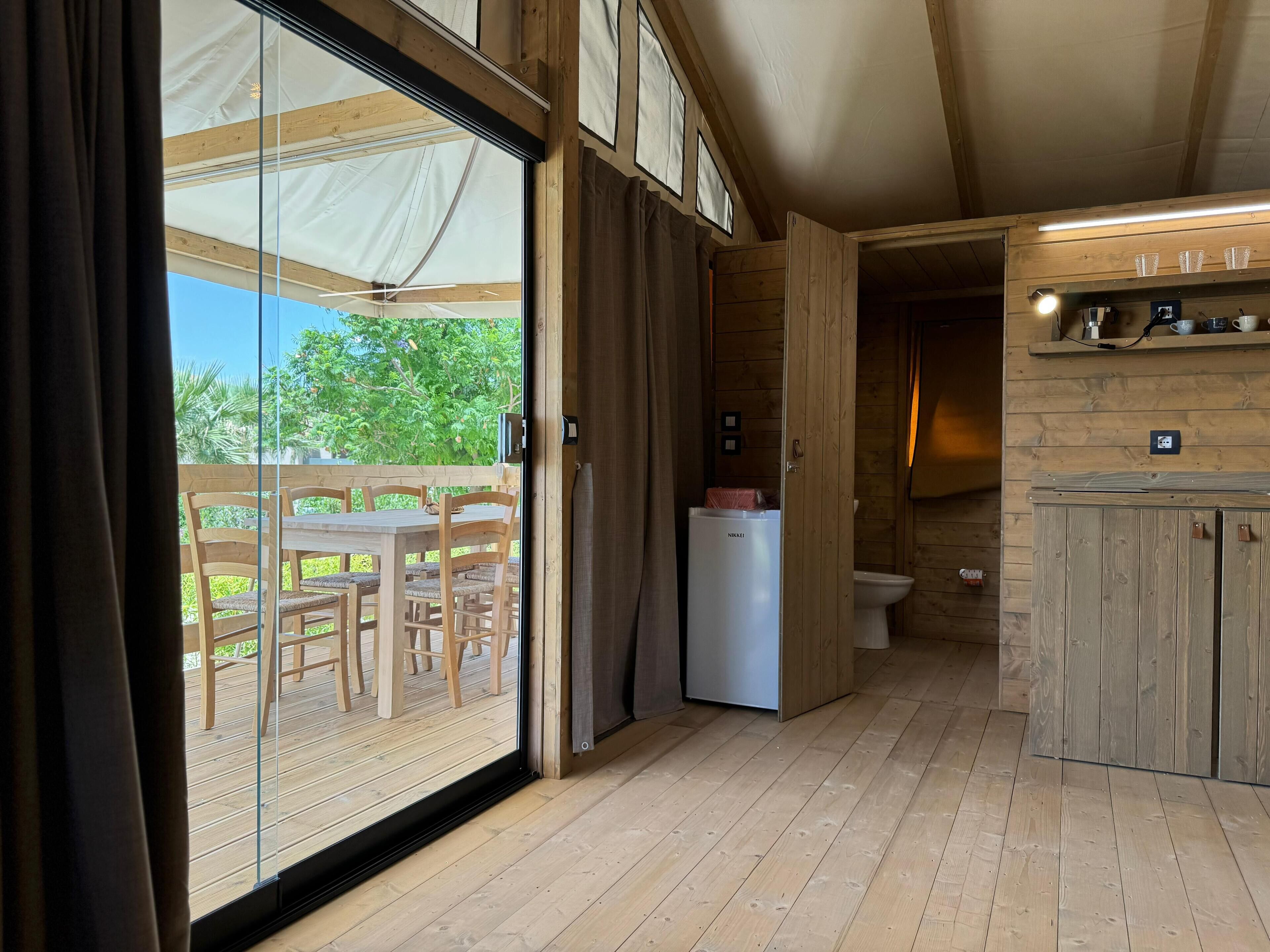 Interior de madera con puerta corredera de vidrio que da a un área exterior, una pequeña kitchenette y una mesa de comedor de madera con sillas.
