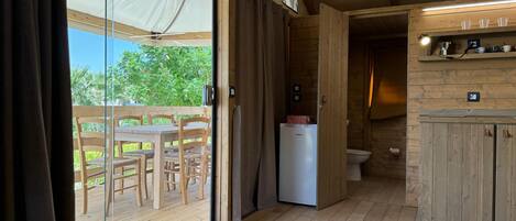 A wooden interior with a sliding glass door leading to an outdoor area, a small kitchenette, and a wooden dining table with chairs.