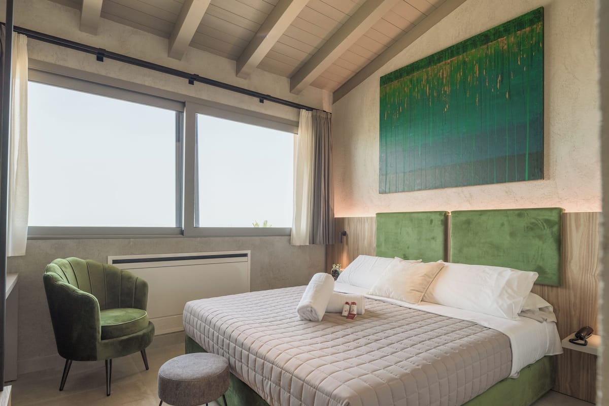 Ein Schlafzimmer mit einem großen Bett, einem grünen Sessel und einem Fenster mit Vorhängen.