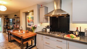 A modern kitchen with a central island, stainless steel appliances, and a large range hood. - The Beach Retreat (Filey)