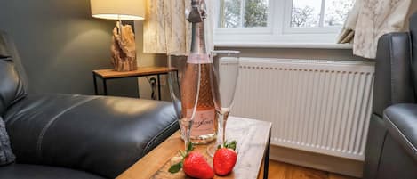 A cozy living room with a leather sofa, a small wooden table with a bottle of Freixenet Italian Rosé, two strawberries, and a glass.