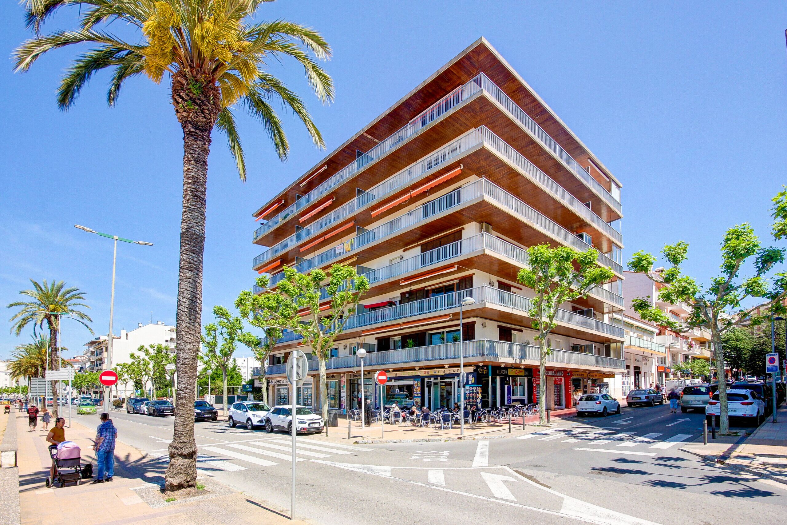 Un edificio a più piani con balconi, un attraversamento pedonale e palme.