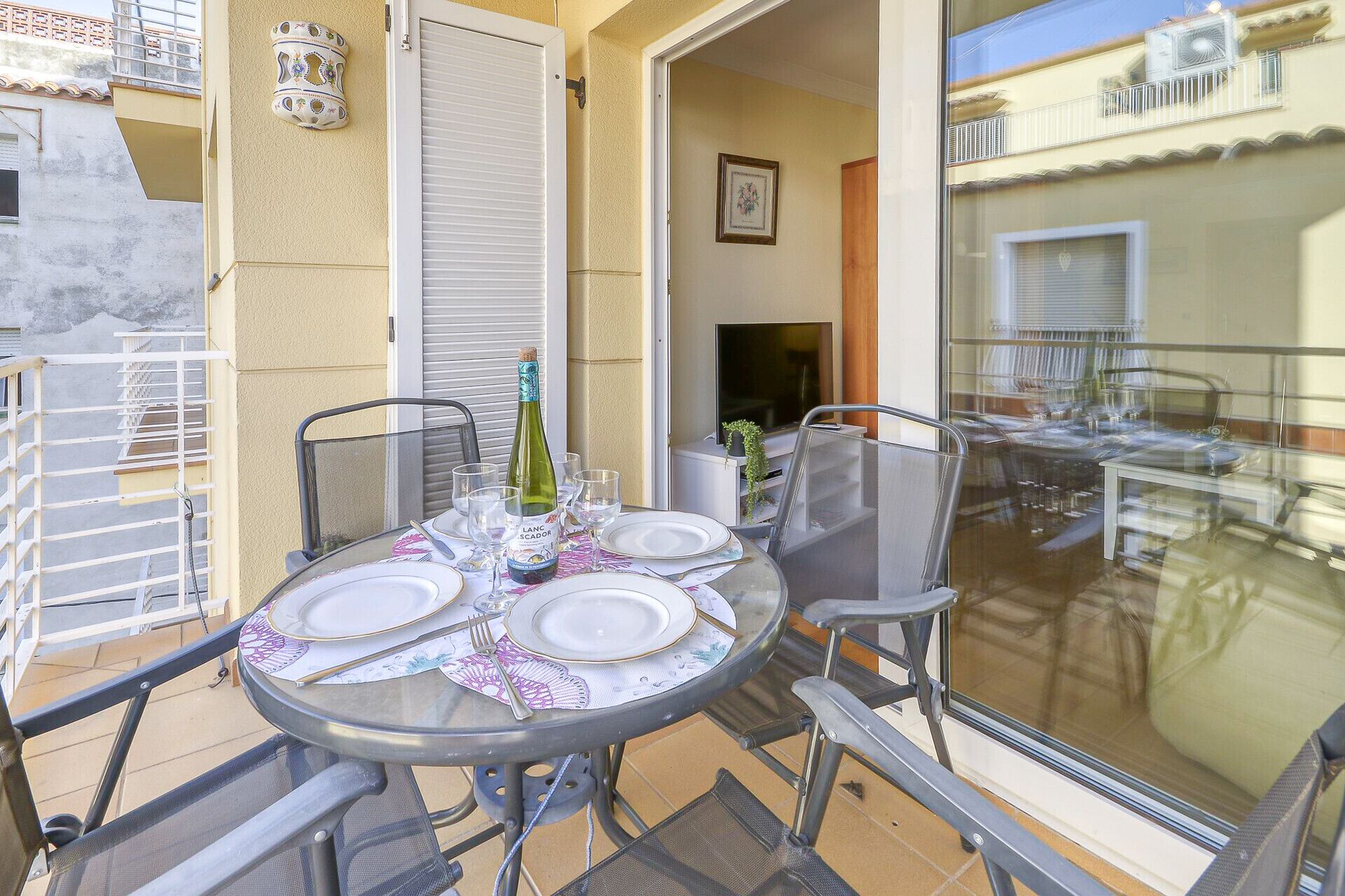 A round table set for four with plates, cutlery, and a bottle of wine, surrounded by chairs.