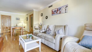 A living room with a beige sofa, a glass coffee table, and a dining area with a wooden table and chairs.