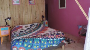 Un dormitorio con pared de paneles de madera, cama con manta colorida, escritorio con lámpara y ventana pequeña.