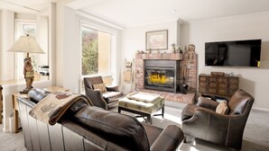 Una sala de estar con sofás de cuero, chimenea, televisor y un amplio ventanal.