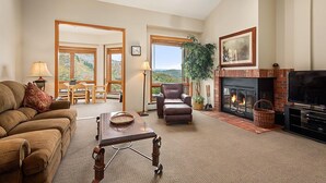 A spacious living room with a fireplace, a television, and a large window offering a mountain view. - Chamonix 37 | Snowmass Ski-In/Ski-Out Condo w/Shared Hot Tub & Pool/Private Washer/Dryer/WiFi (Snowmass Village)