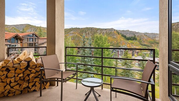 A balcony with a view of a mountainous landscape, a stack of firewood, and two chairs and a small table. - Chamonix 37 | Snowmass Ski-In/Ski-Out Condo w/Shared Hot Tub & Pool/Private Washer/Dryer/WiFi (Snowmass Village)
