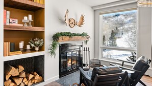 Ein gemütliches Wohnzimmer mit Kamin, Bücherregalen und Blick auf eine verschneite Landschaft.