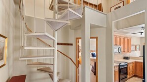 Un intérieur moderne avec un escalier en colimaçon, un espace de vie et une cuisine à aire ouverte, et des meubles de rangement en bois.