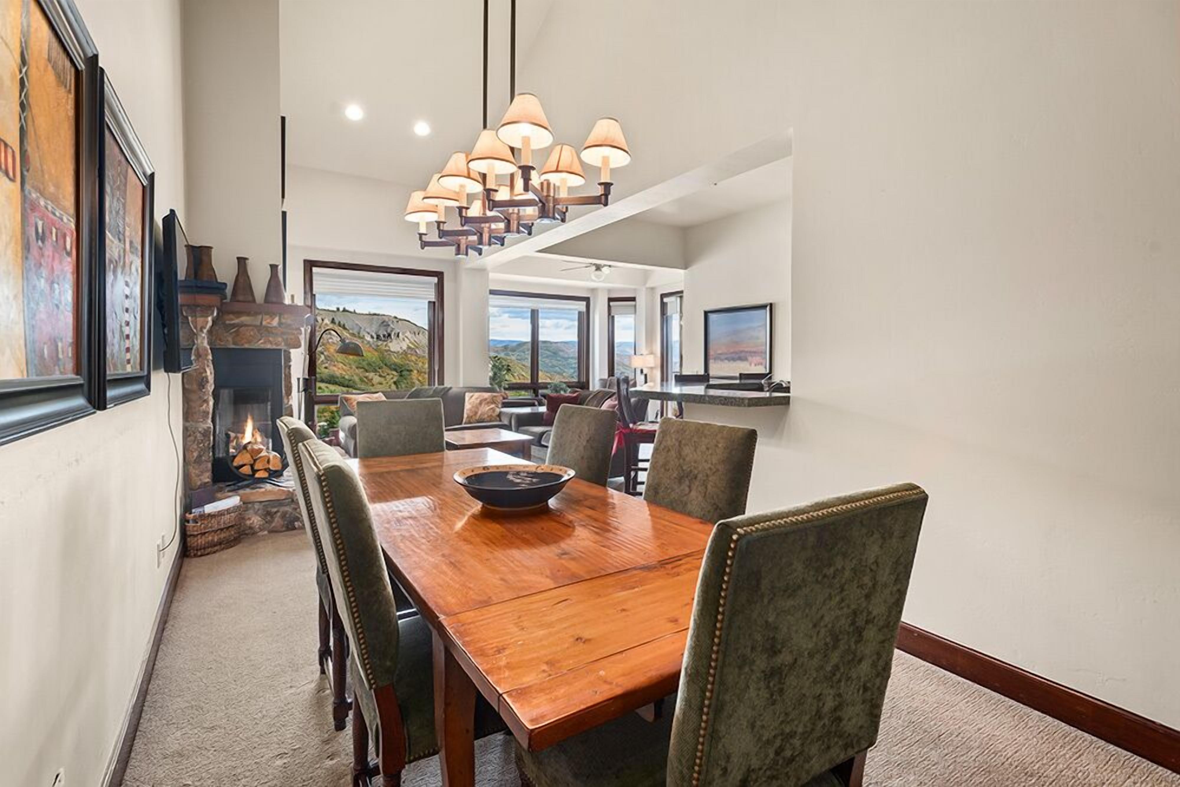 A dining area with a wooden table, chairs, a fireplace, and a large window offering a scenic view.
