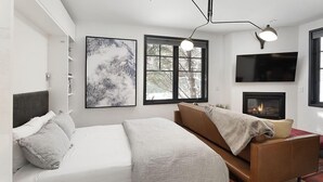 A modern bedroom with a bed, a sofa, a fireplace, and a large window. - Christiana Lodge 102A | Studio in Aspen with Hot Tub access (Aspen)