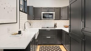 A modern kitchen with dark cabinets, a white countertop, a stainless steel microwave, and a sink. - Christiana Lodge 102A | Studio in Aspen with Hot Tub access (Aspen)