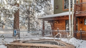 A wooden cabin with a stone hot tub, surrounded by snow-covered trees and a metal fence. - Christiana Lodge 102A | Studio in Aspen with Hot Tub access (Aspen)