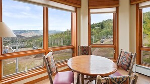 A room with a round wooden table and chairs, large windows with wooden frames, and a view of a mountainous landscape. - Chamonix 54 | Snowmass Ski-In/Ski-Out Condo with Pool, Hot Tub, Free WiFi, & Airport Shuttle (Snowmass Village)