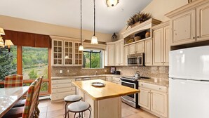A kitchen with a central island, white cabinets, and a view of the outdoors. - Chamonix 54 | Snowmass Ski-In/Ski-Out Condo with Pool, Hot Tub, Free WiFi, & Airport Shuttle (Snowmass Village)