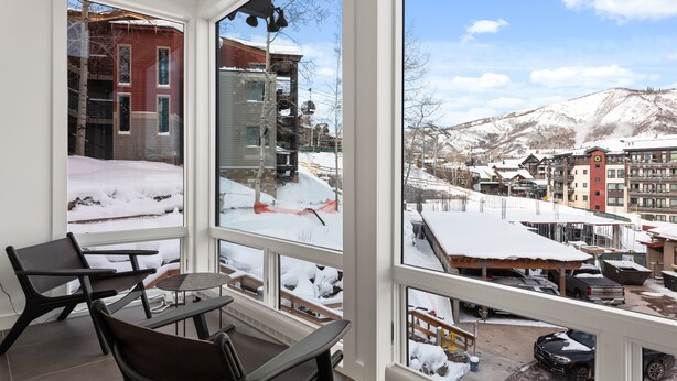 A room with a large window offering a view of a snowy mountain town, a dining area with a table and chairs, and a visible heater. - Enclave 102 | Snowmass Ski-In/Ski-Out Condo w/Shared Pool/Hot Tub (Snowmass Village)