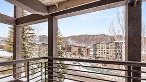 A balcony with a metal railing overlooking a construction site and buildings in a mountainous area. - Enclave 201 | Snowmass Ski-In/Ski-Out Condo w/Shared Pool/Hot Tub/Gym/WiFi (Snowmass Village)