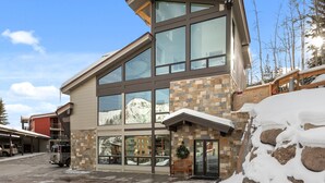 A multi-story building with large windows, a stone facade, and a snow-covered ground. - Enclave 201 | Snowmass Ski-In/Ski-Out Condo w/Shared Pool/Hot Tub/Gym/WiFi (Snowmass Village)